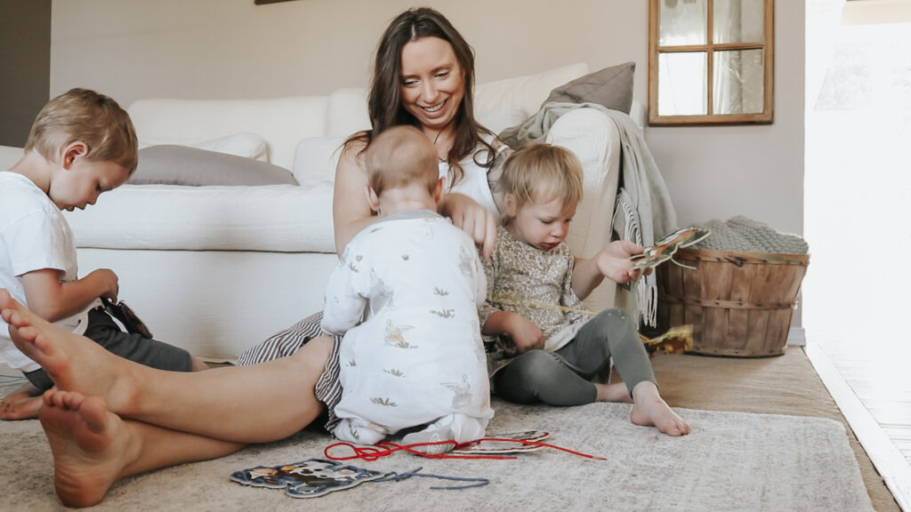 Christian homemaker plays on the ground with her 3 small children, she is smiling and enjoying her time with her children